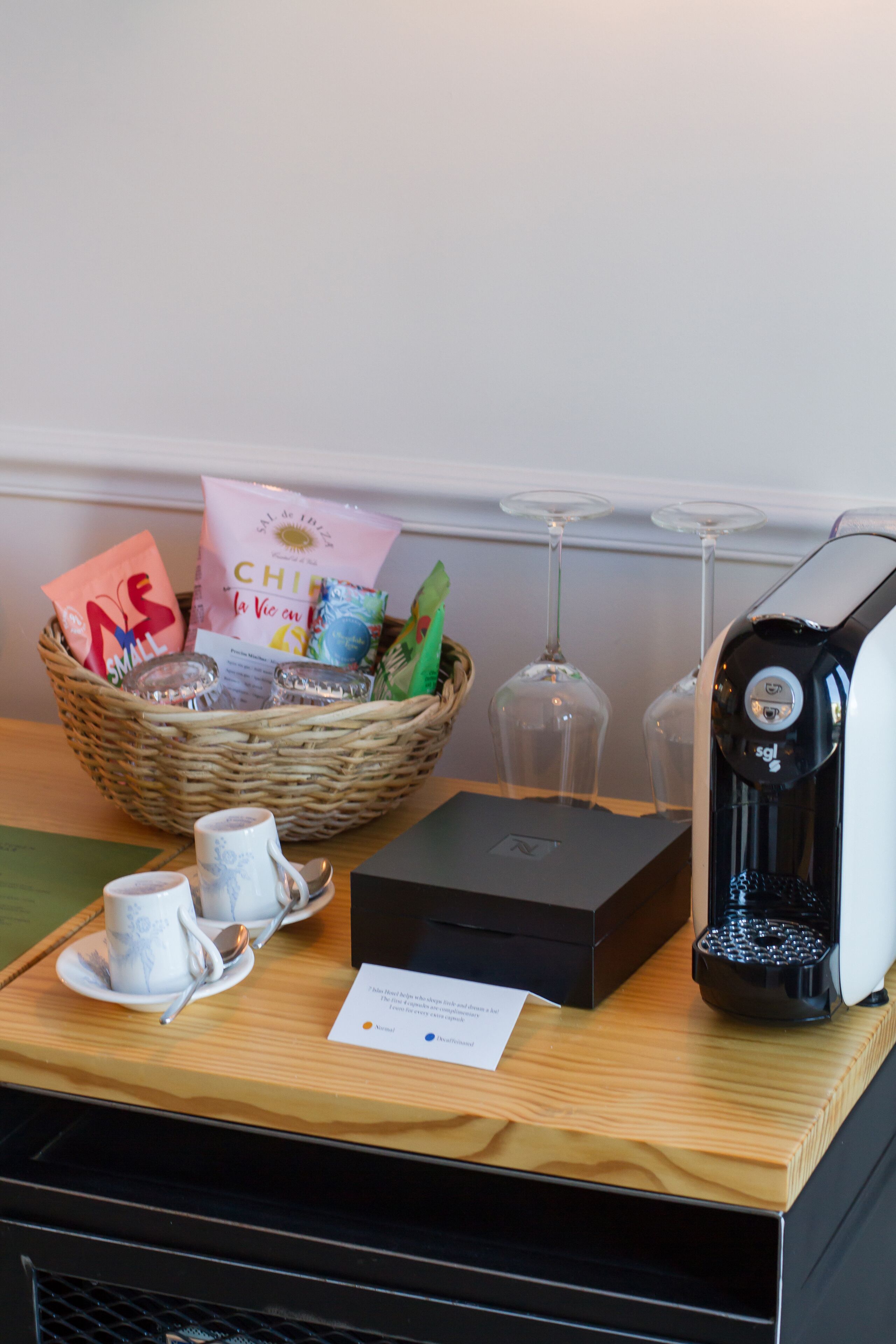 A breakfast setup with a basket of snacks, a coffee maker, and two cups on a tray.