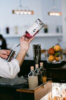 Ein Barkeeper gießt ein Getränk aus einer Flasche in einen Shaker.