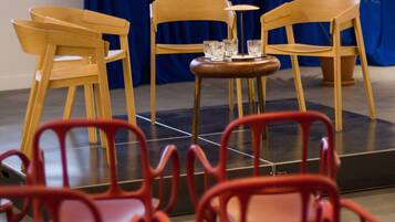 Un escenario con un telón de fondo azul, sillas de madera y una pequeña mesa con vasos.