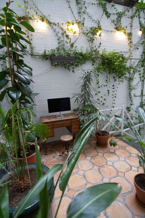 A small workspace with a desk, computer, and potted plants.
