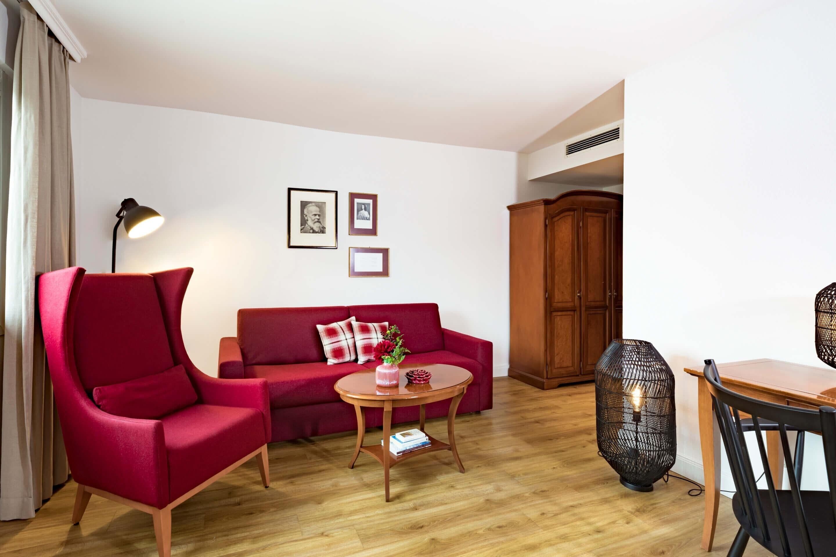Un salon moderne avec un canapé rouge, une table basse ronde en bois, un fauteuil noir, une lampe et un meuble.