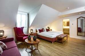 Ein modernes Schlafzimmer mit Schräge, einem großen Bett, einer Sitzecke mit einem roten Sessel, einem kleinen runden Tisch mit Dekoration und einem großen Spiegel an der Wand.
