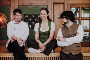 Three people sitting on a wooden bench in a room with wooden walls and a green chalkboard. - Hotel Prinzregent München (Munich)