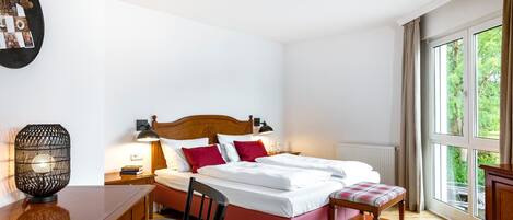 A bedroom with a wooden bed, a desk, a chair, a lamp, and a window with a view of greenery.