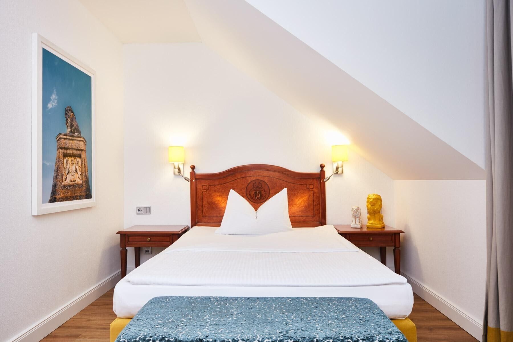 A bedroom with a wooden headboard, two bedside lamps, a bed with white linens, a blue throw blanket, and a framed picture on the wall.