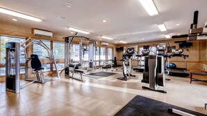 Een sportschool met diverse trainingsapparaten, grote ramen en een houten inrichting.