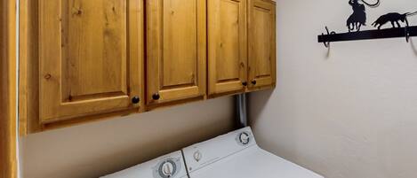 Un área de lavandería con armarios de madera y una lavadora y secadora blancos.