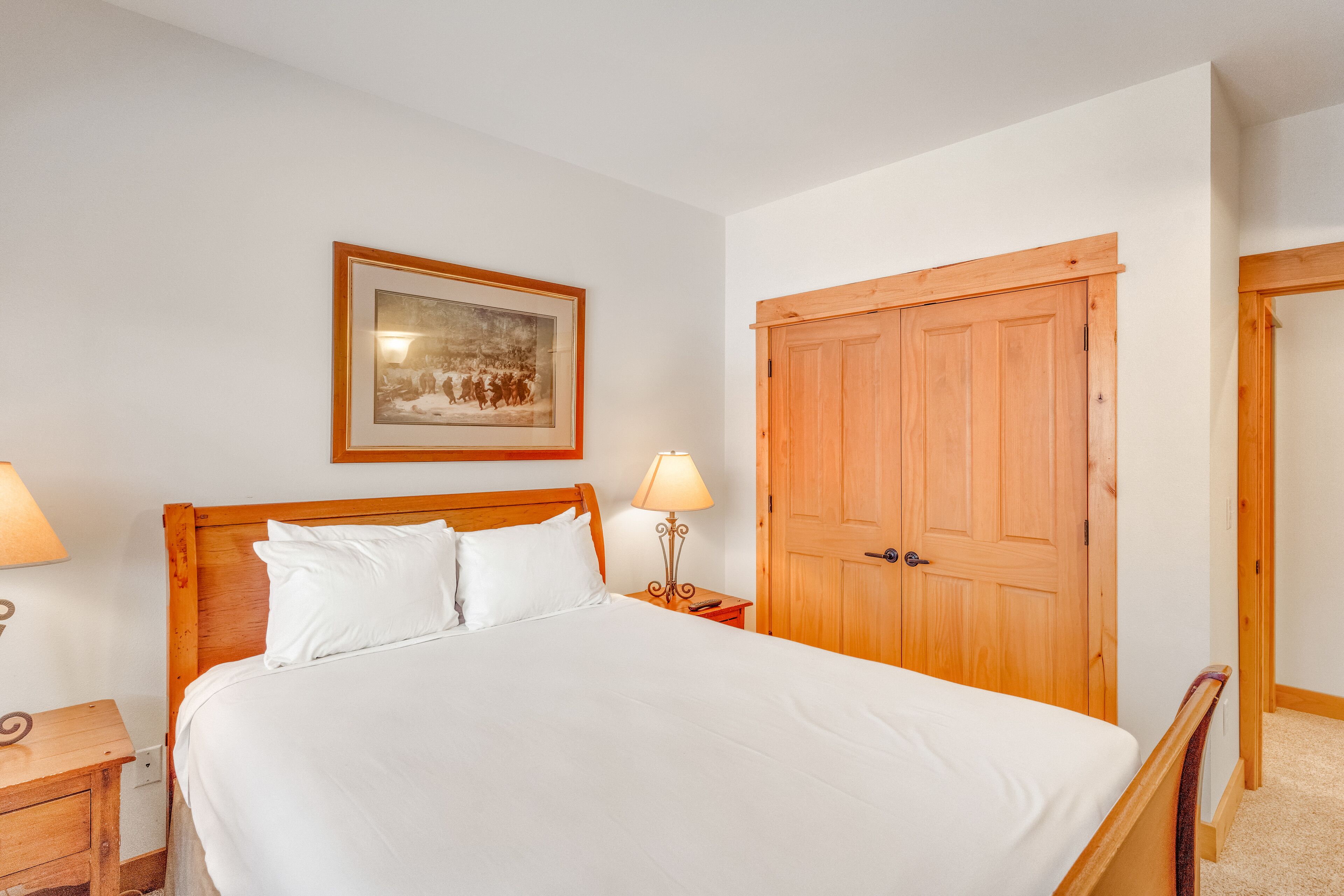 A neatly made bed with white linens, a wooden headboard, and two bedside lamps.