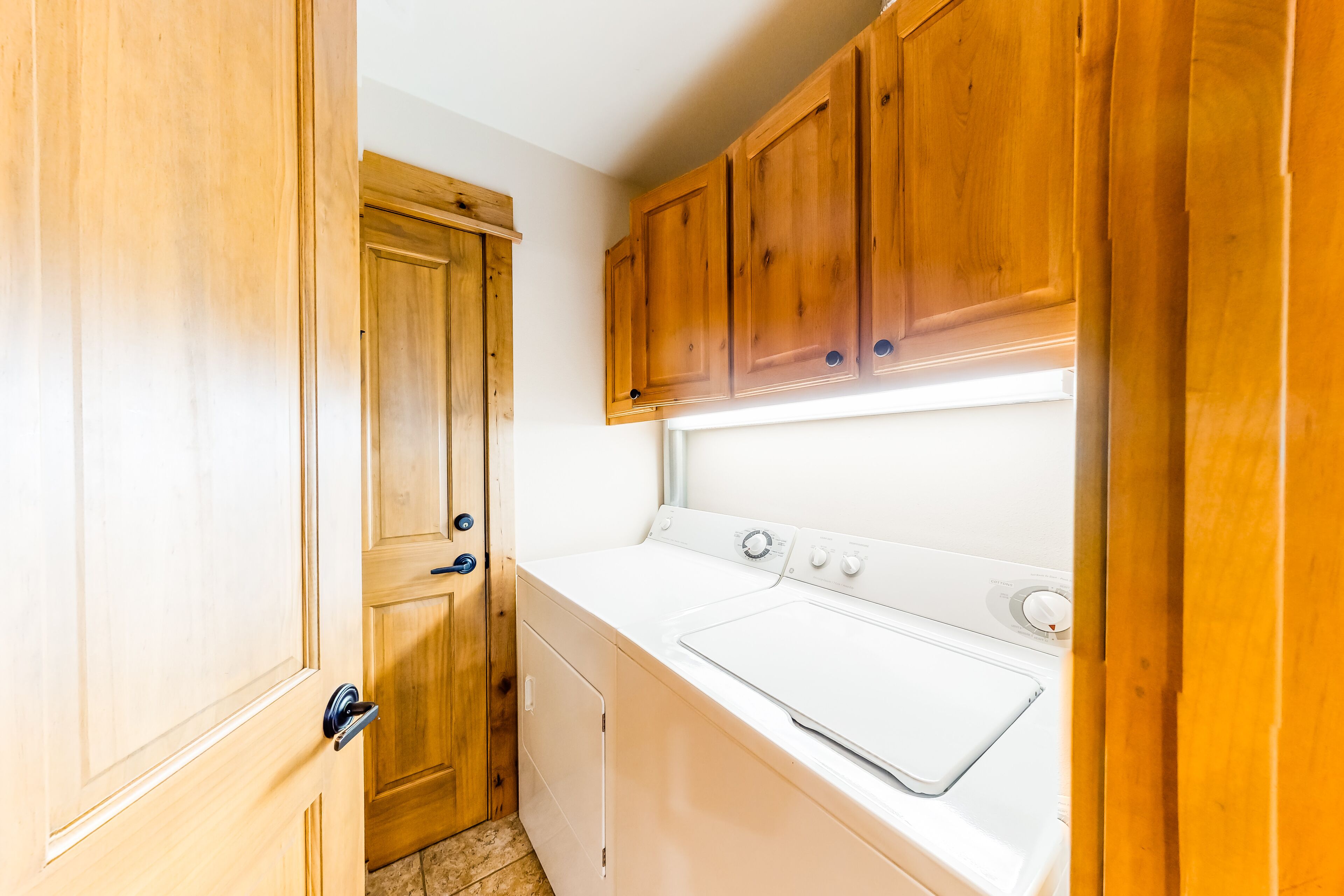 A compact kitchen with wooden cabinets, a built-in washer and dryer, and a door leading to another room.