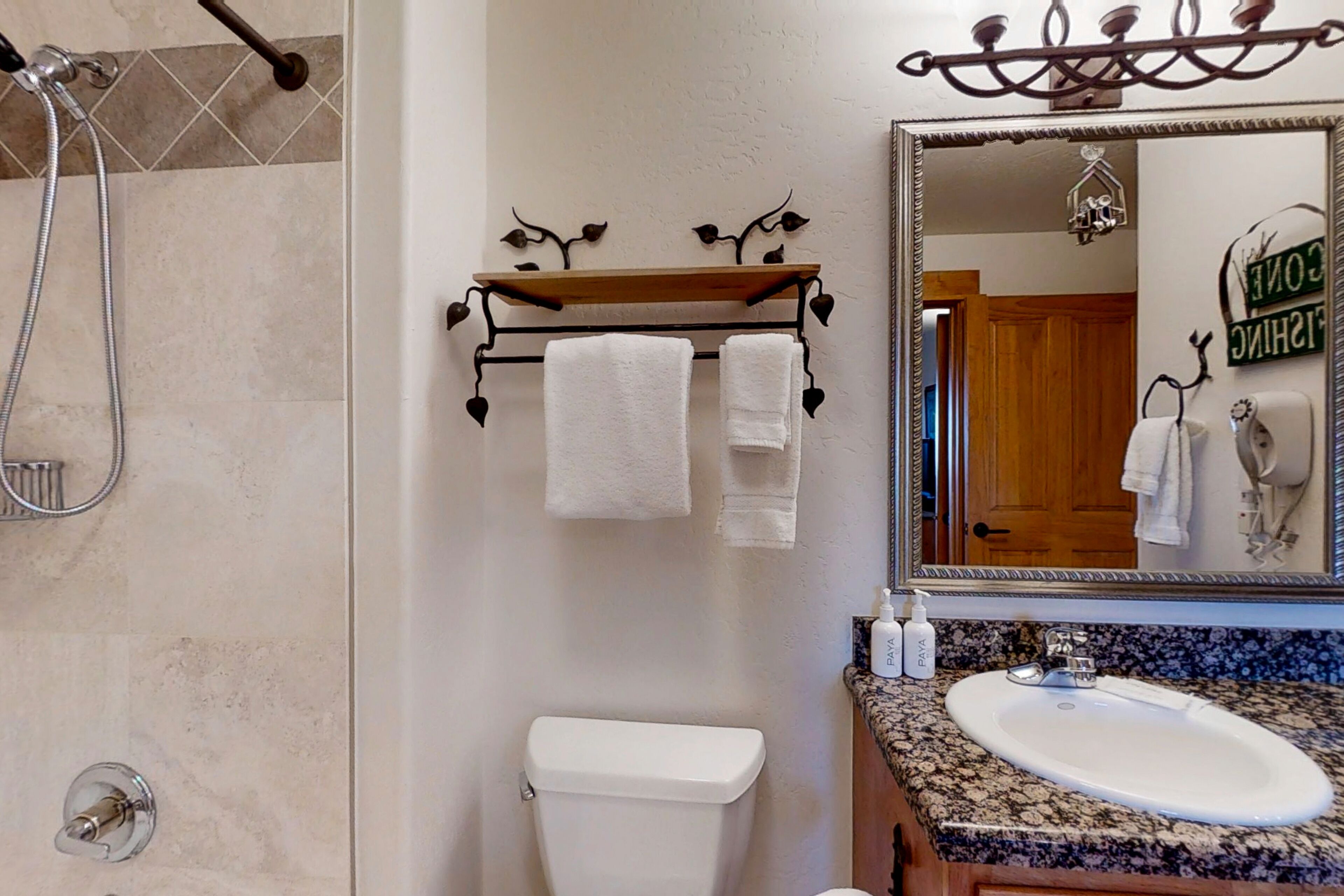 A bathroom with a shower, toilet, sink, and a mirror with a decorative frame.