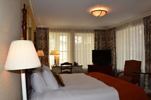 Een hotelkamer met een groot bed, een bureau met lamp, een stoel, een televisie en gordijnen.