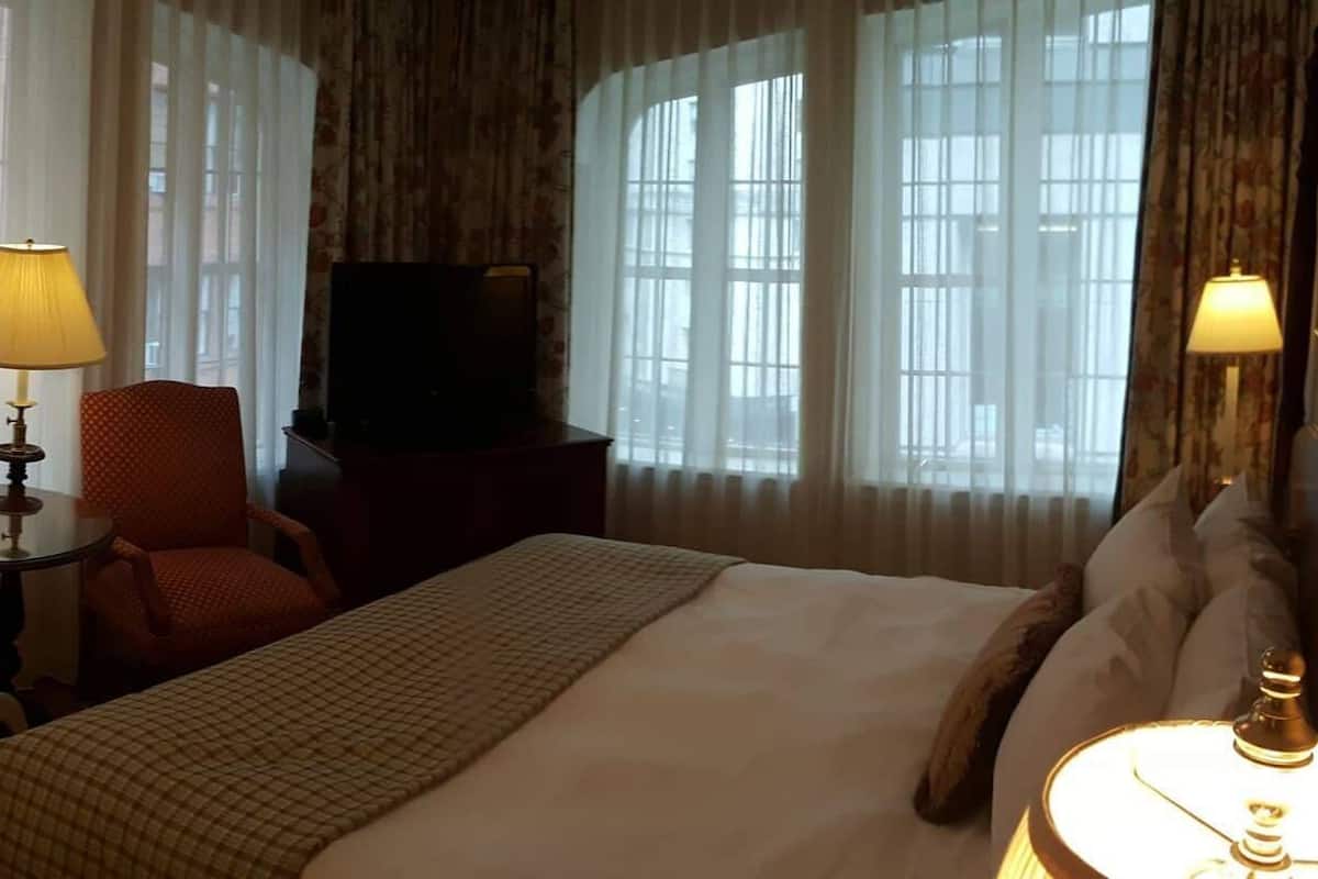 A hotel room with a bed, two chairs, a small table, a TV, and lamps.
