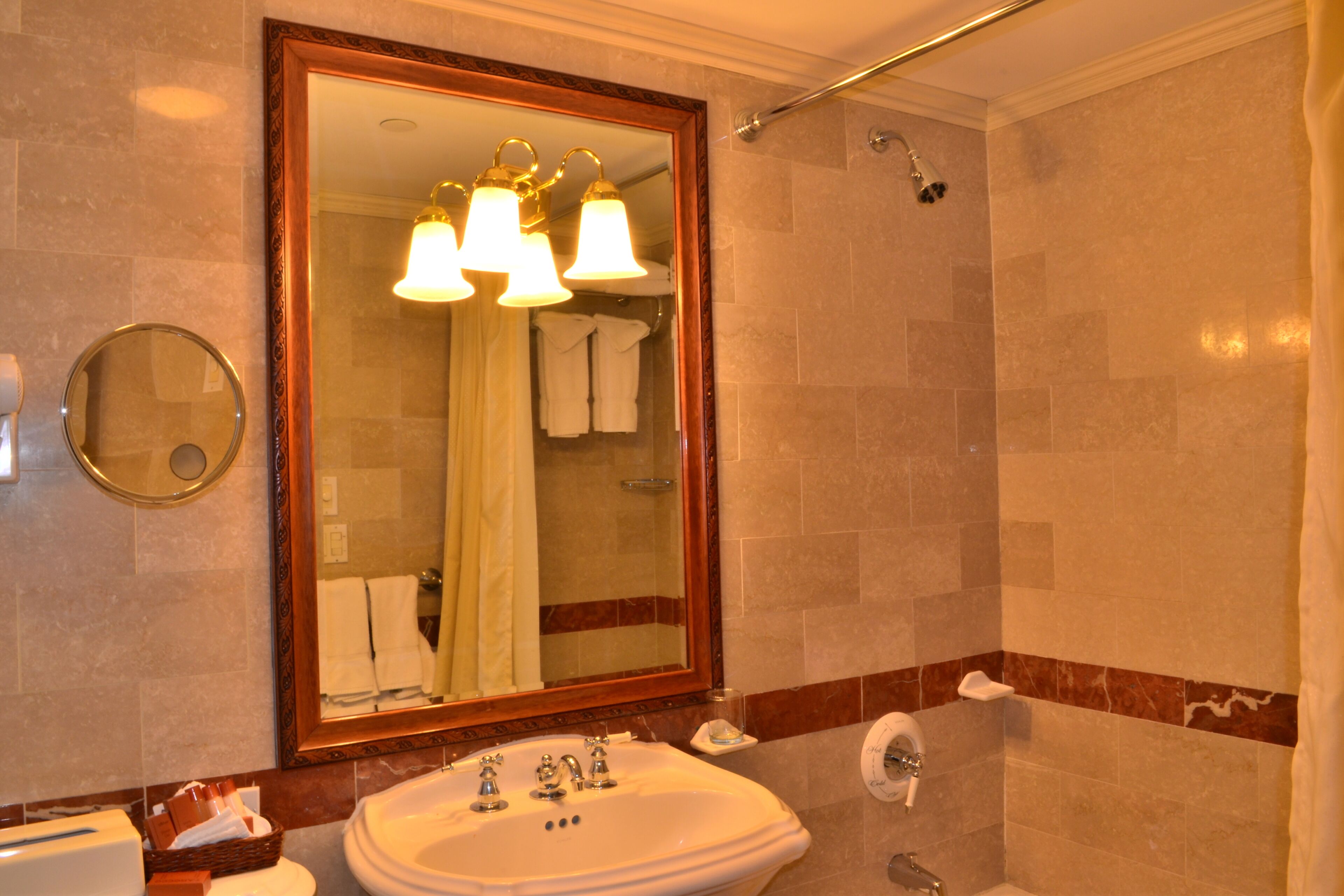 A bathroom with a large mirror, a sink, a shower, and a towel rack.