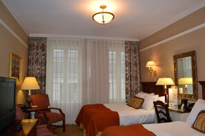 A hotel room with two beds, a desk with a lamp, a chair, a television, and a large mirror. - The Wall Street Inn (New York)