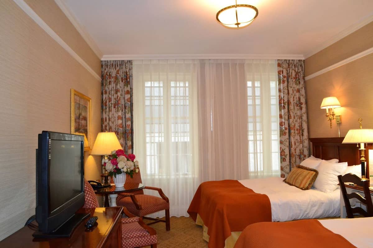 A hotel room with a bed, two bedside tables, a desk with a television, a chair, and a window with curtains.