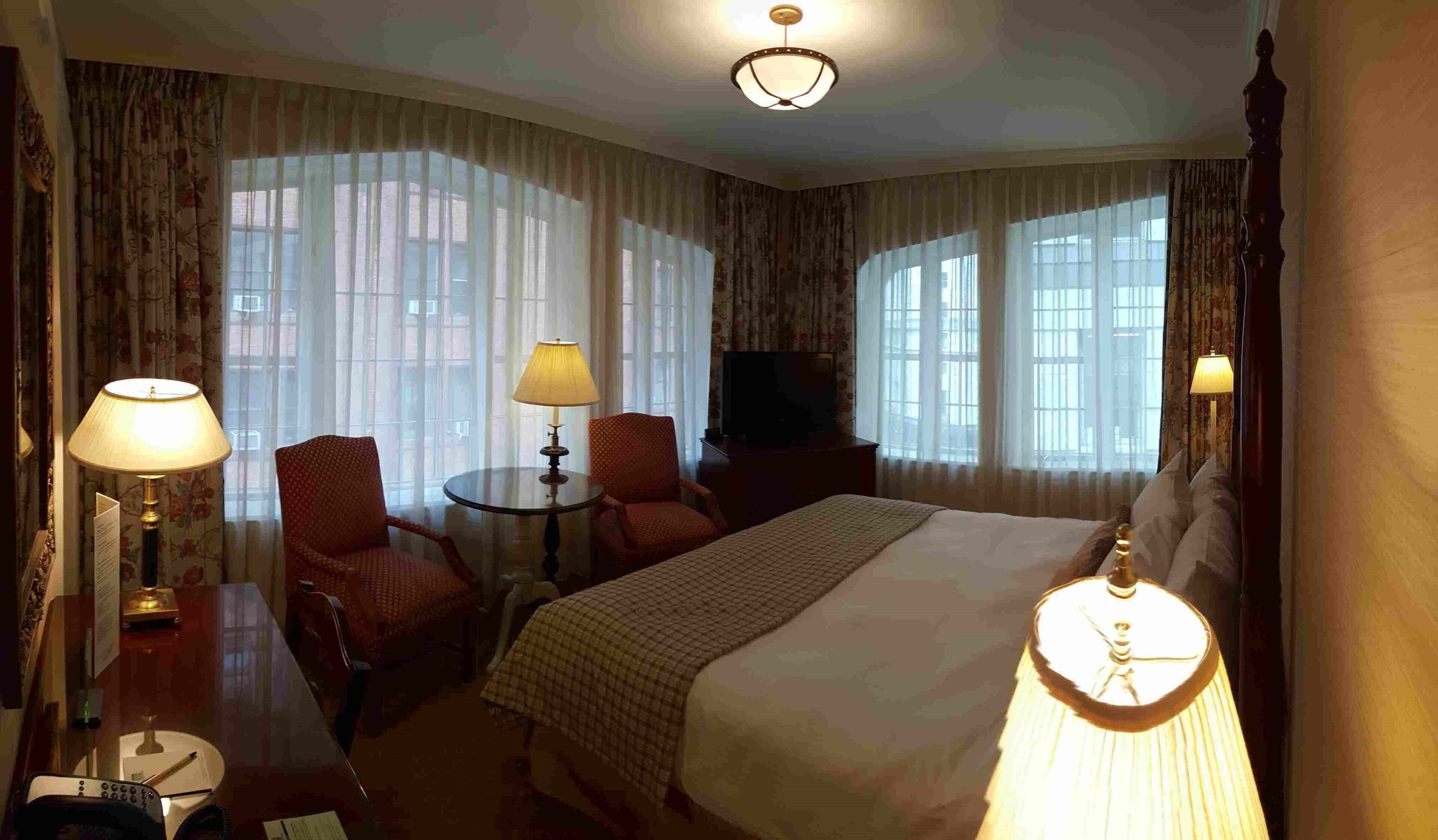 A hotel room with a large bed, two armchairs, a small table, a TV, and a lamp.