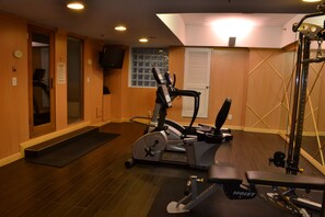A home gym with exercise equipment, a door, a window, and a wall-mounted TV. - The Wall Street Inn (New York)