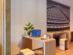 A modern office space with a laptop, a potted plant, and a coffee cup on a wooden desk. - ibis Lorient Centre Gare (Lorient)