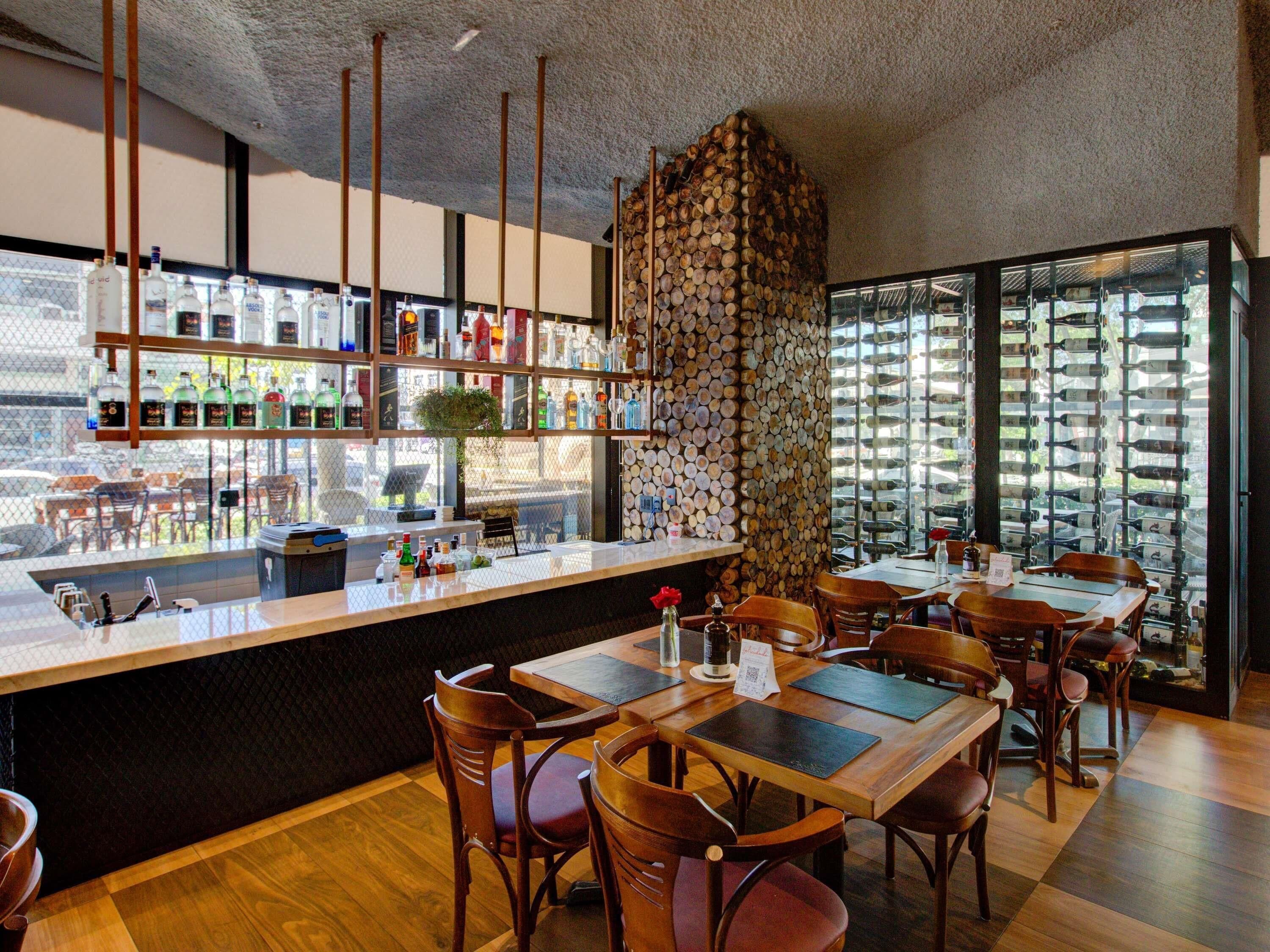A restaurant with a bar area, wooden tables, and chairs.
