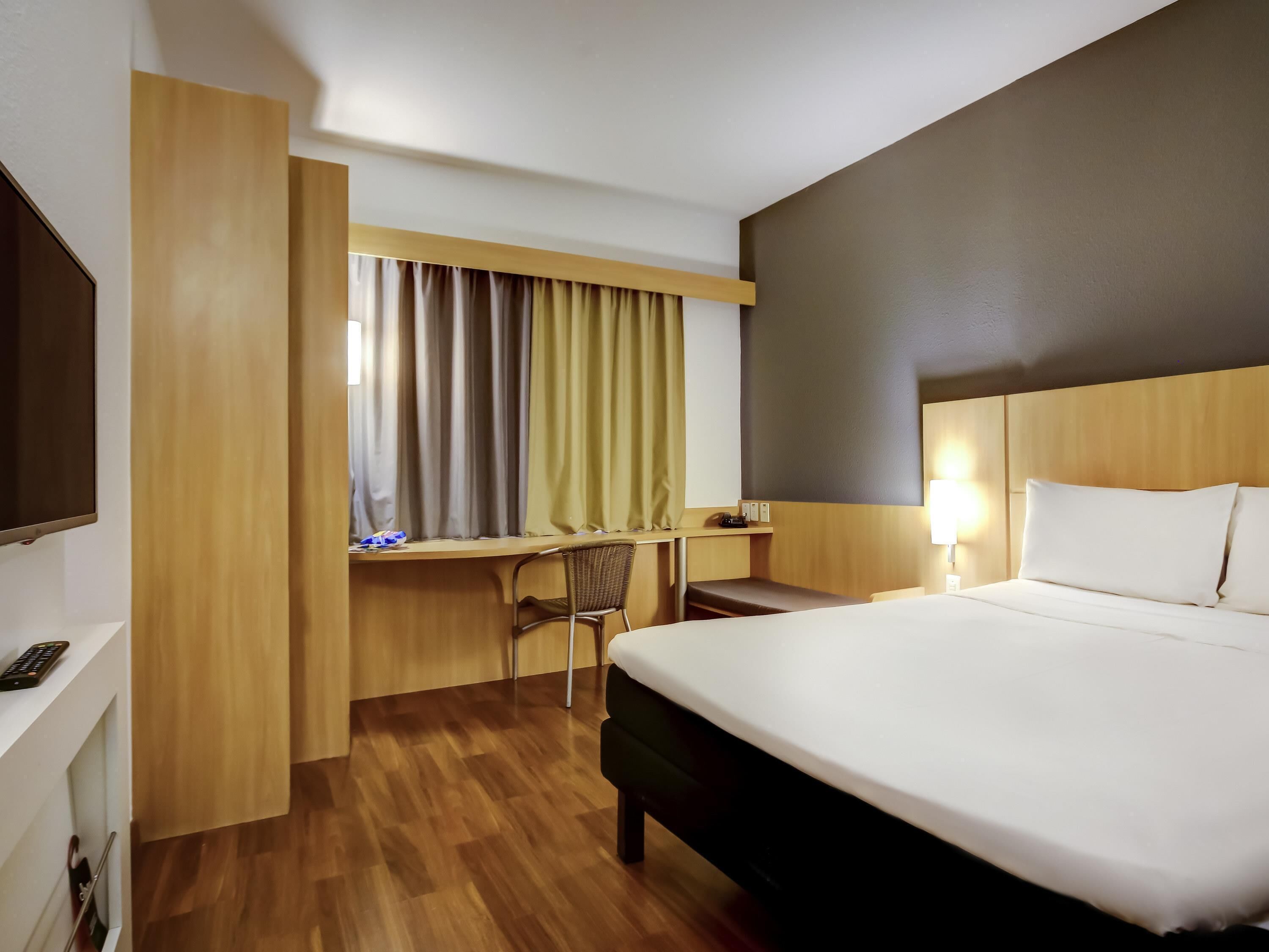 Habitación de hotel con cama, escritorio, silla y televisor.