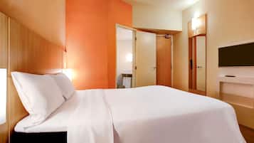 Une chambre d’hôtel avec un lit, une télévision, une armoire et une salle de bain visible à travers une porte ouverte.