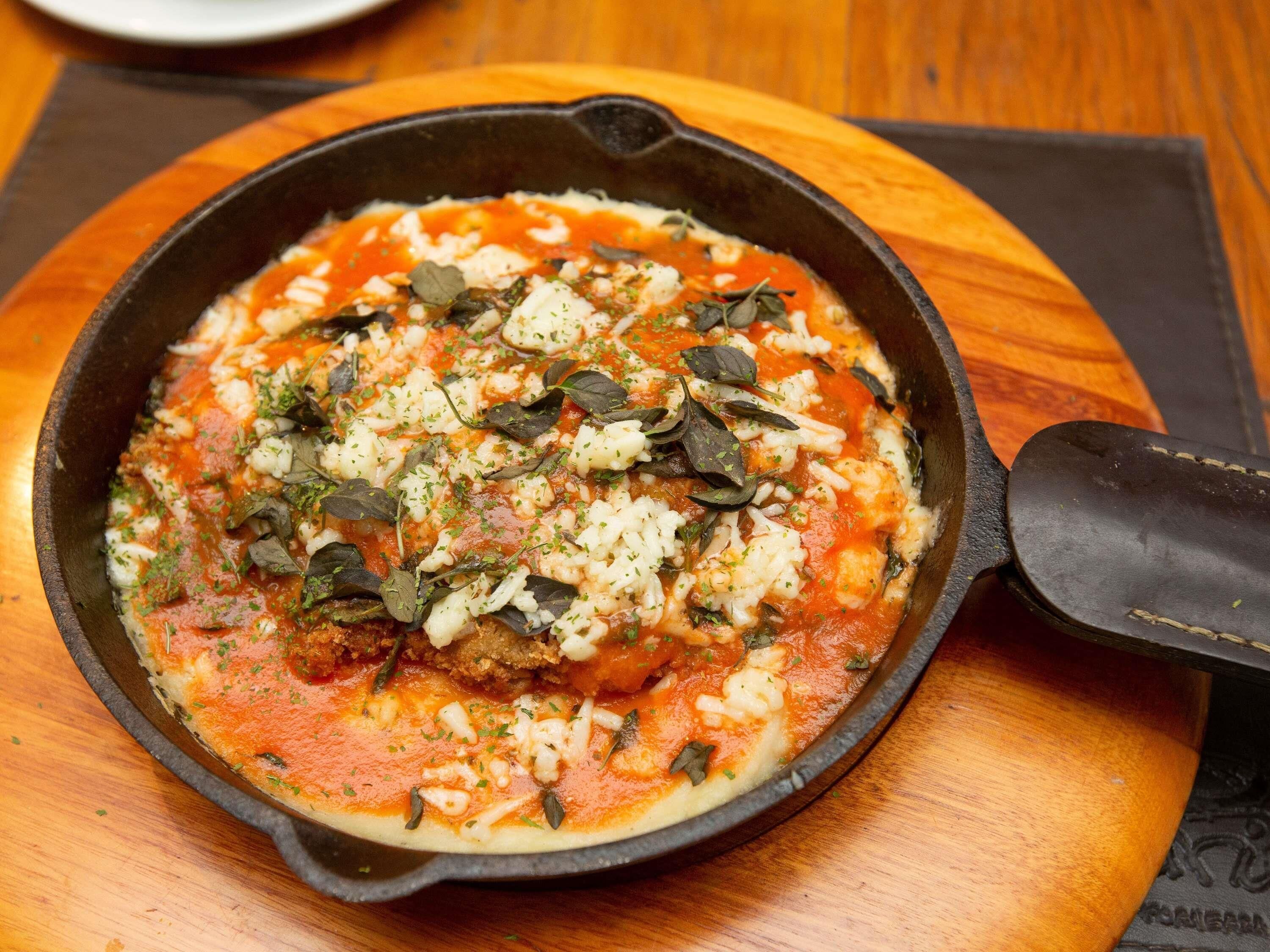 Una sartén con un plato que lleva salsa de tomate, queso y hierbas.