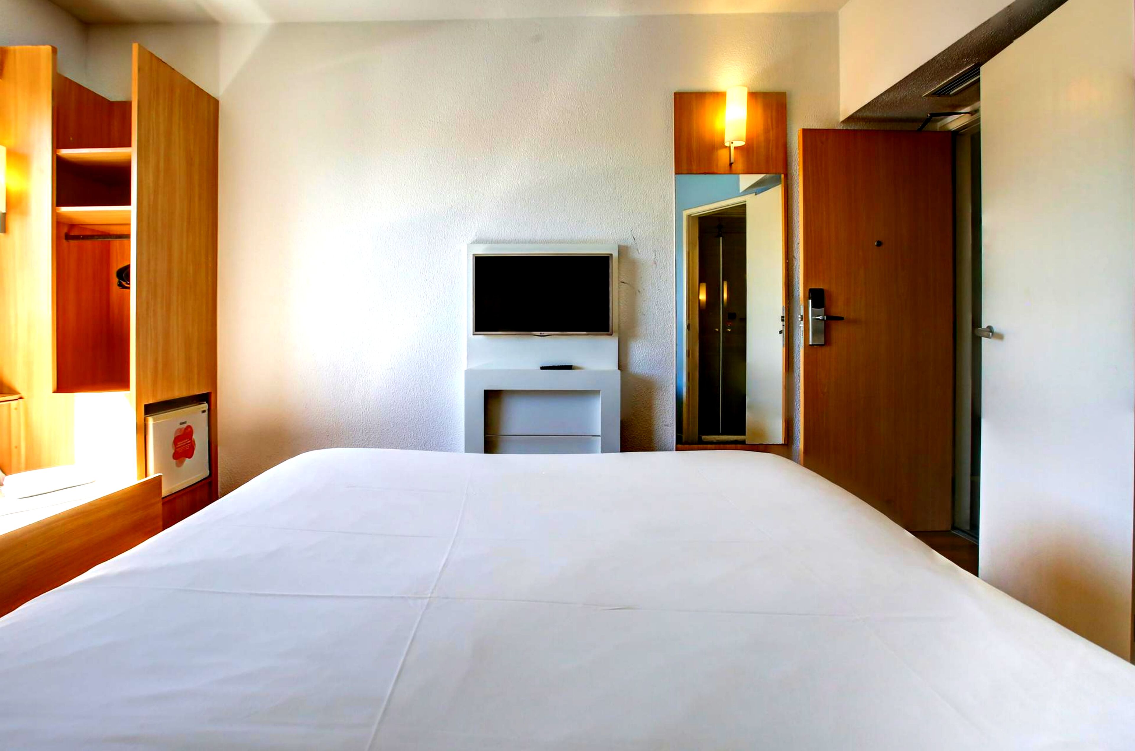 Quarto de hotel com cama, televisão, guarda-roupa e espelho.