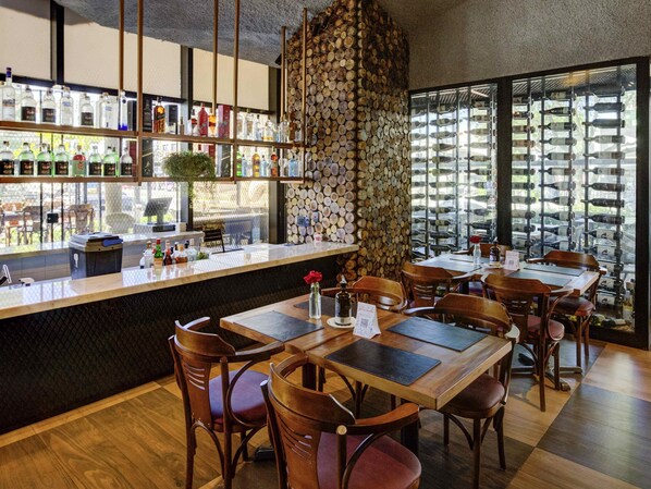 A restaurant with a bar area, wooden tables, and chairs, and a wall of stacked wine bottles. - ibis Vitoria Praia Do Canto (Vitoria)