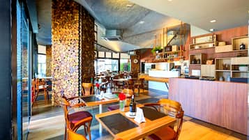 Restaurante moderno com mobiliário de madeira, parede de pedra e área de cozinha visível ao fundo.