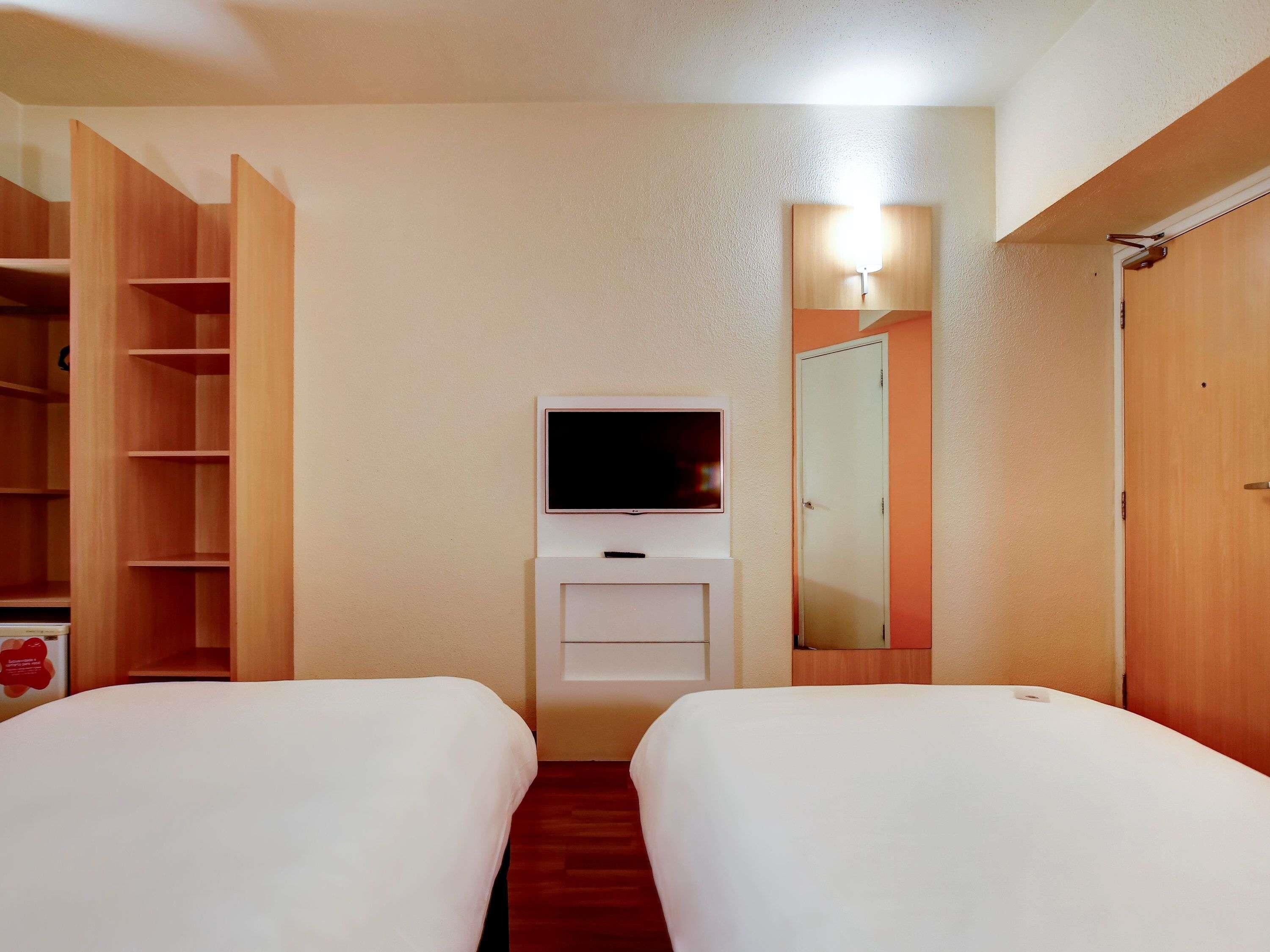 Habitación de hotel con dos camas, televisión, espejo y armario.