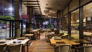 An indoor dining area with wooden tables and wicker chairs, large windows, and a brick wall. - ibis Vitoria Praia Do Canto (Vitoria)