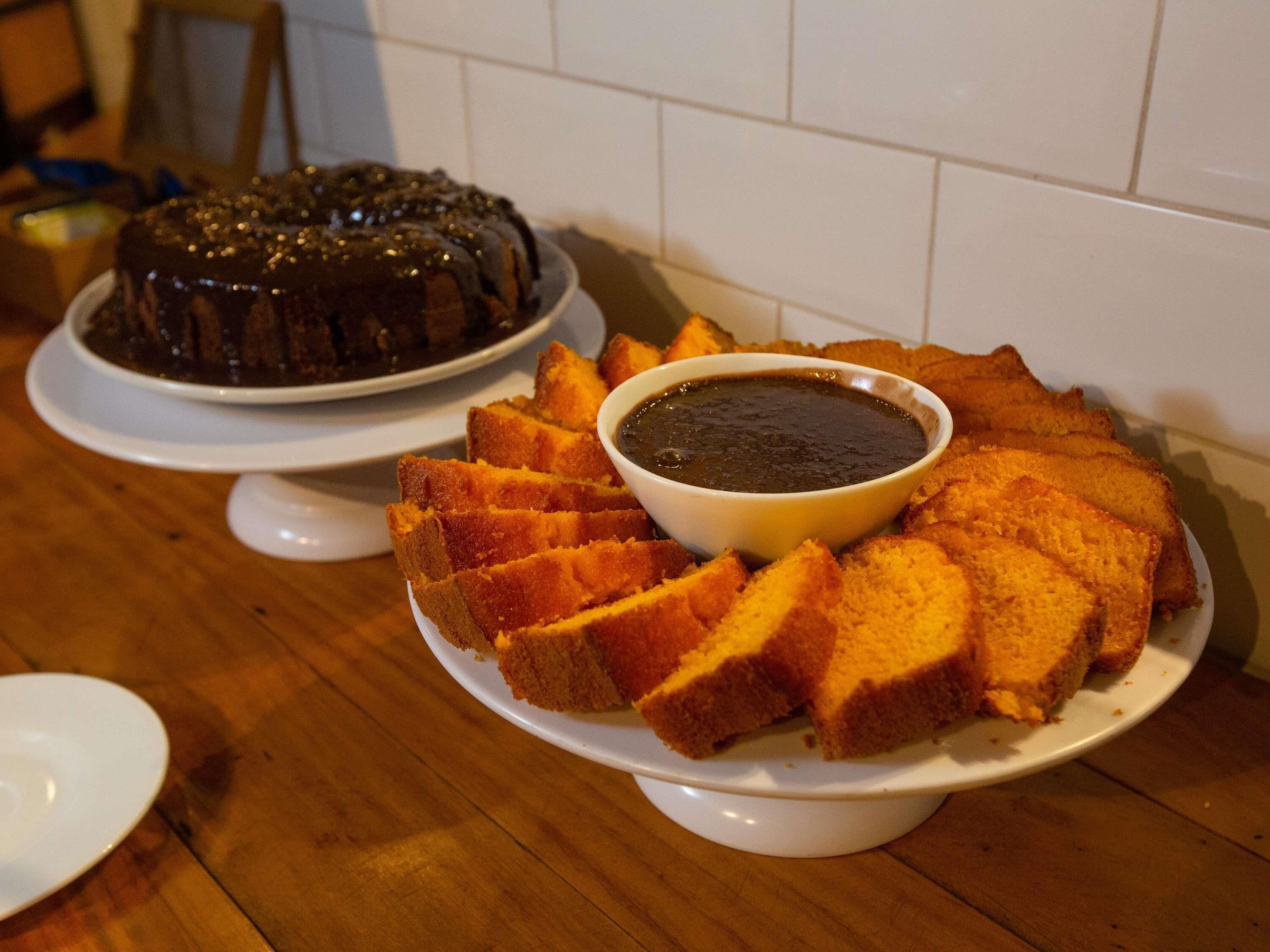 A cake with a chocolate glaze and a bowl of sauce on a wooden table.