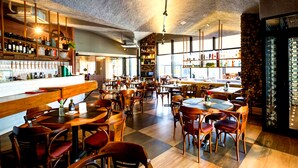 A spacious restaurant with wooden tables and chairs, a bar area with shelves of bottles, and large windows allowing natural light. - ibis Vitoria Praia Do Canto (Vitoria)