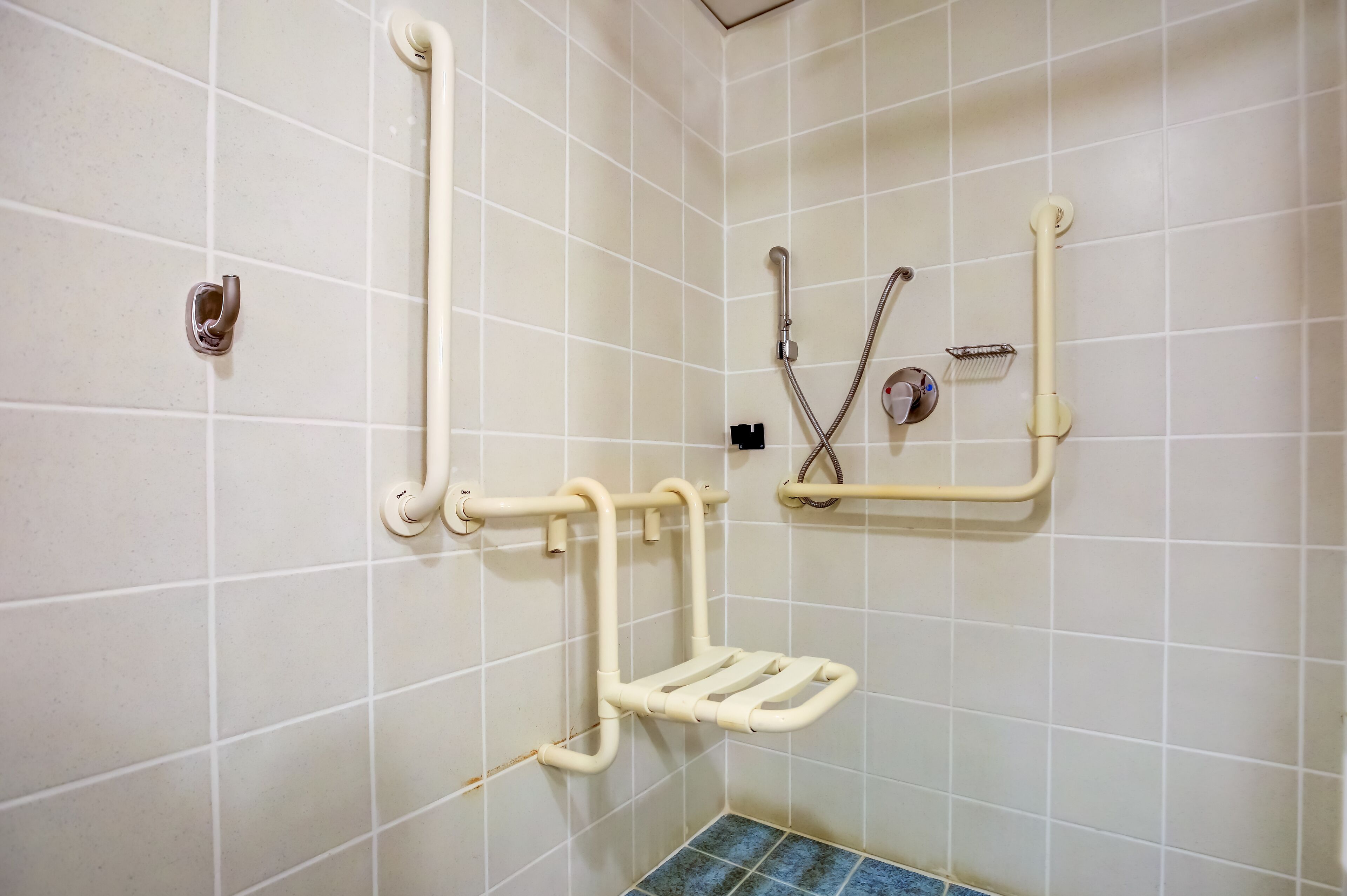 A bathroom with white tiled walls, a blue-tiled floor, and a handrail.