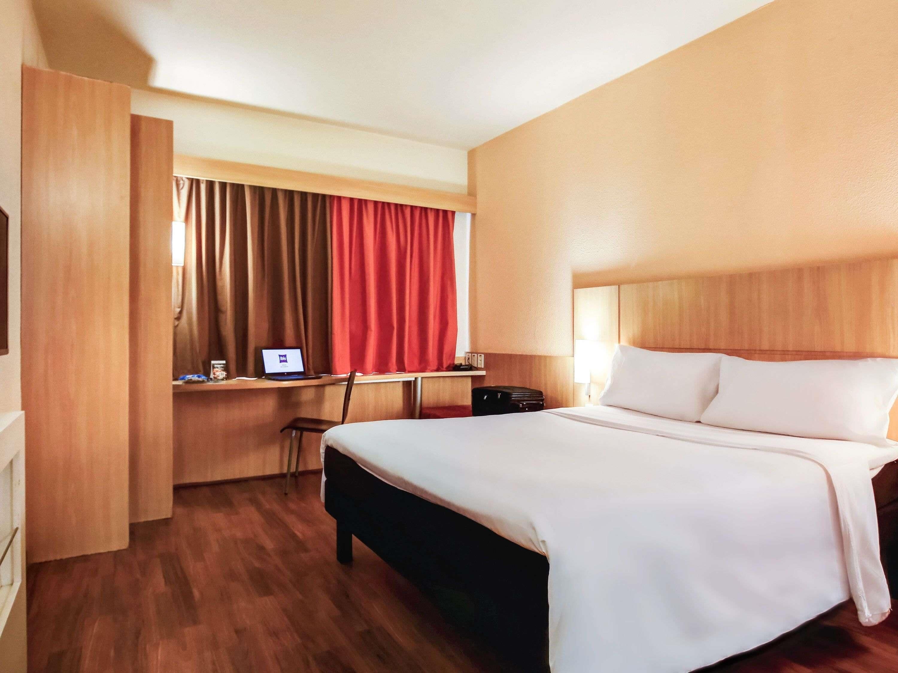 Hotellihuone, jossa on sänky, työpöytä kannettavalla tietokoneella, tuoli ja matkalaukku.