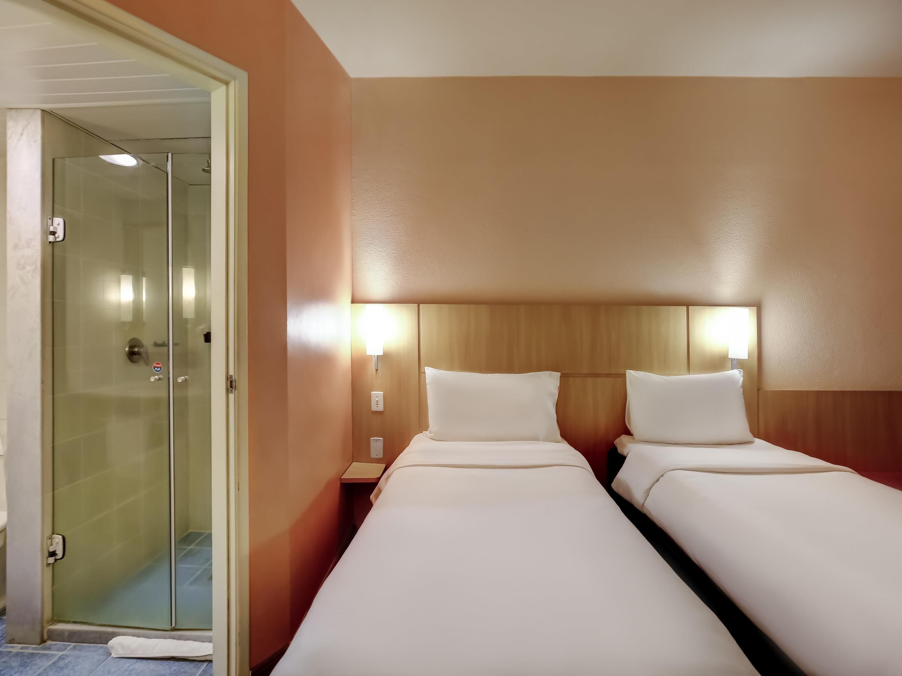 Ein Hotelzimmer mit zwei Betten, einer Glasdusche und einem hölzernen Kopfteil.