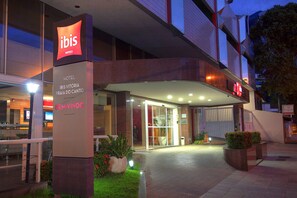 Exterior do hotel ibis, com uma placa grande, entrada de vidro e área de acesso bem iluminada.