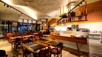 A restaurant with wooden tables and chairs, a counter with a cash register, and a brick wall.