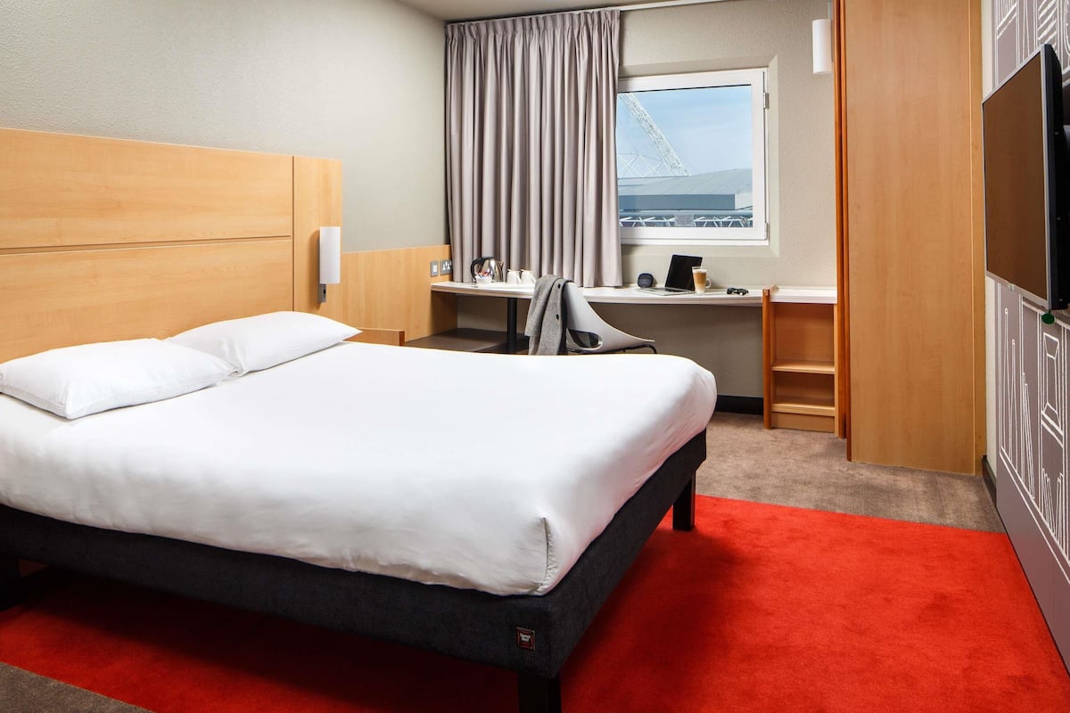A hotel room with a large bed, a desk, a chair, a TV, and a window with a view of a bridge.