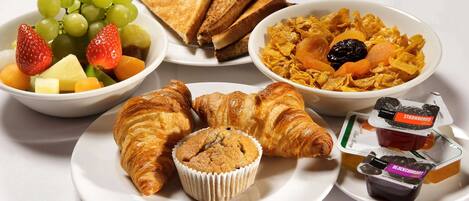 A breakfast spread with croissants, muffins, toast, fruit, cereal, and yogurt.
