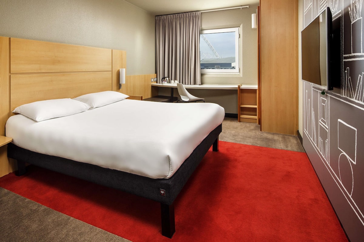 A hotel room with a bed, desk, chair, and a TV.