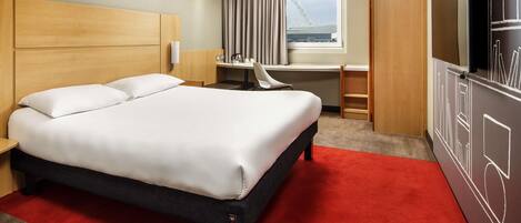 A hotel room with a bed, desk, chair, and a TV.