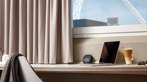A hotel room with a view of a Ferris wheel, a laptop, a smartphone, a glass of coffee, and a herringbone-patterned throw blanket. - ibis London Wembley (Wembley)