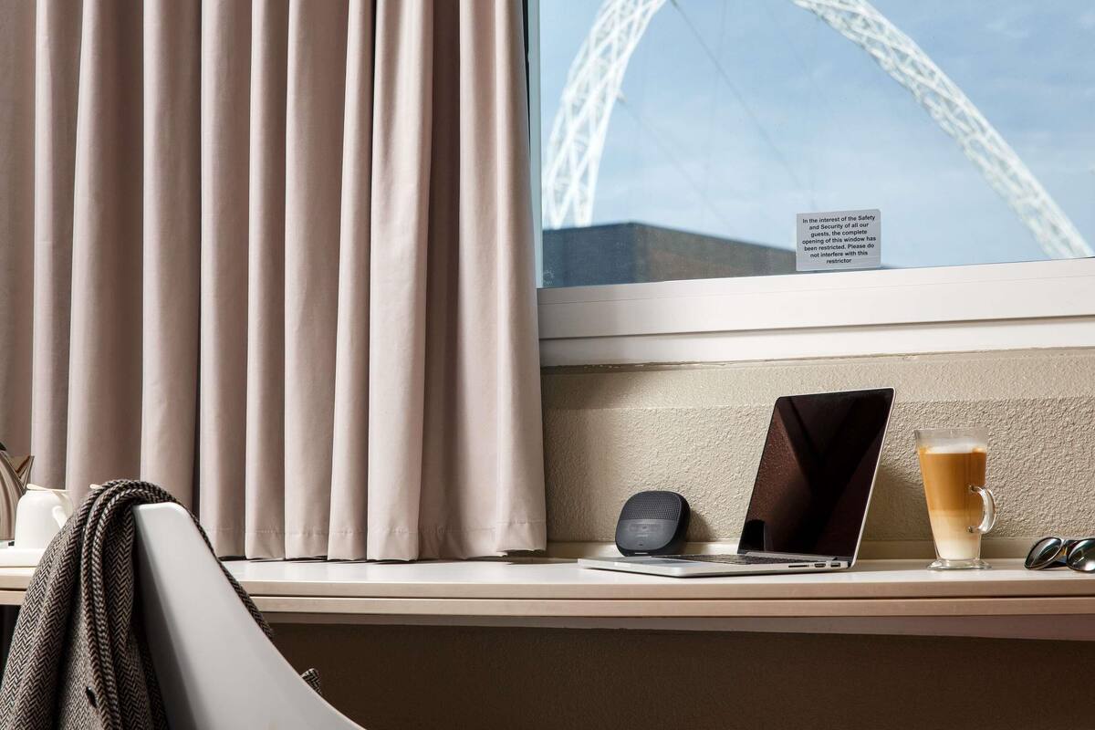 Une chambre d’hôtel avec vue sur une grande roue, un ordinateur portable, un téléphone intelligent, une tasse de café et un plaid à motifs chevrons.