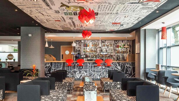A modern bar area with a patterned wall and red accents, surrounded by black and white patterned seating. - ibis London Wembley (Wembley)