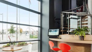 A modern interior with a large window, a computer screen displaying 'Free Internet', and a wooden counter with red chairs. - ibis London Wembley (Wembley)
