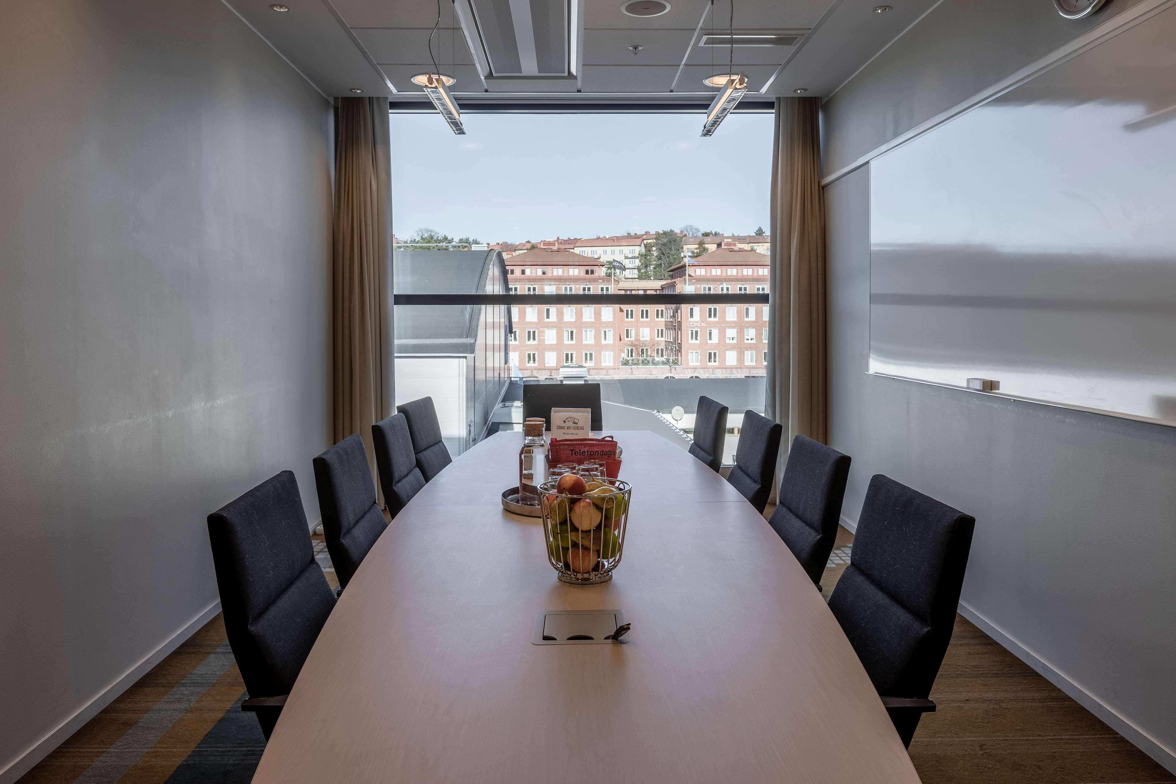Un salón de conferencias con una larga mesa, sillas y una cesta decorativa de frutas.