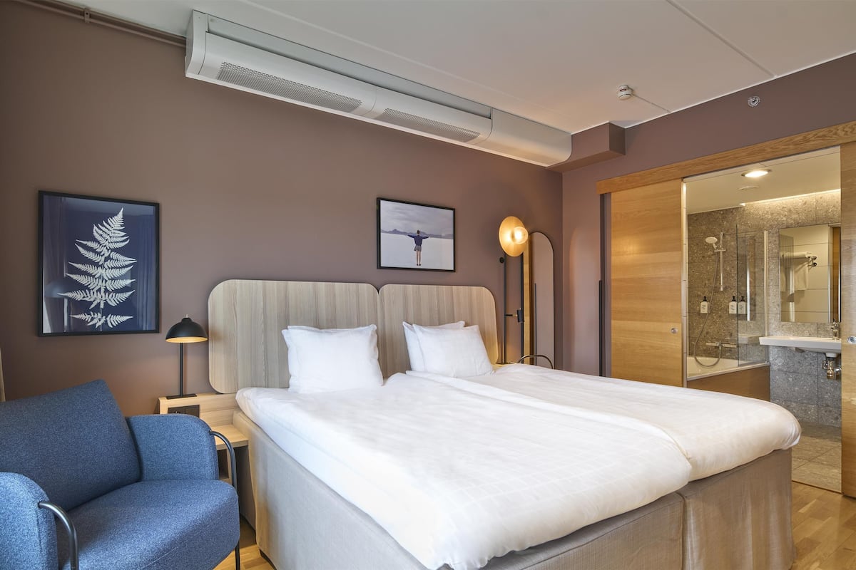 Une chambre d’hôtel avec un grand lit, une chaise, un bureau et une salle de bain visible à travers une porte ouverte.