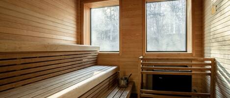A wooden sauna with benches and a sauna table, large windows, and a tiled floor.
