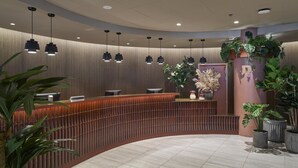A modern reception area with a curved wooden reception desk, multiple pendant lights, and various potted plants. - Scandic Alvik (Bromma)